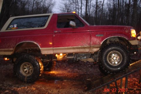 1995 Ford Bronco - A lifted red Ford Bronco navigates an off-road course in muddy conditions.