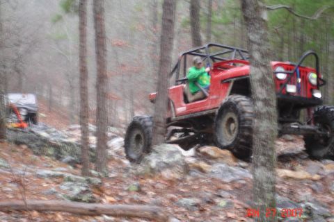 1995 Ford Bronco - A red off-road vehicle tackles a challenging rocky path in a forest setting.