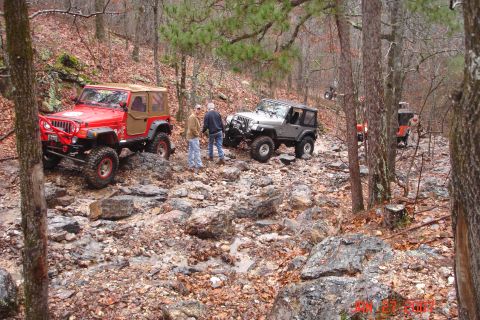 1995 Ford Bronco - Several Jeeps navigate a challenging, rocky trail through a forest in winter.