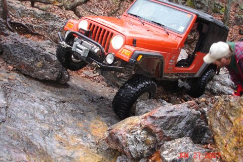1995 Ford Bronco - Jeep Wrangler TJ tackling a challenging rocky trail with a person observing.