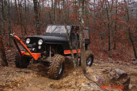 1995 Ford Bronco - A modified Jeep navigates a muddy trail through a forest with fallen leaves.