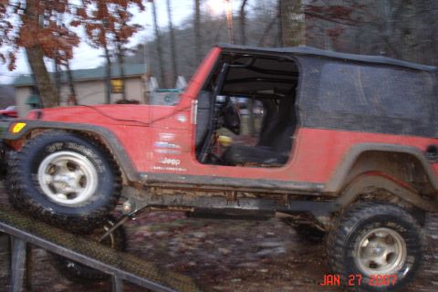 1995 Ford Bronco - A red Jeep Wrangler is shown in profile, with its doors and soft top removed, navigating an off-road obstacle.