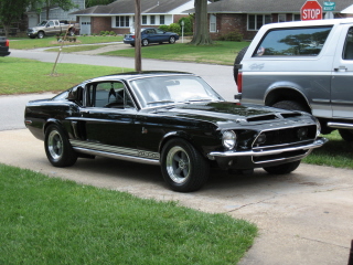 1968 Shelby GT500 - This black 1968 Shelby GT500 is parked on a driveway, showing its distinctive body style and side stripes.