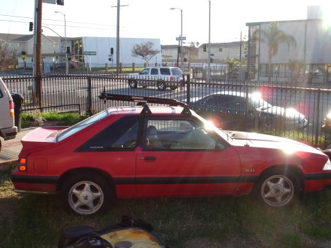 1993 Ford Taurus - Side view of a red coupe with a roof rack, likely a Ford Mustang from the early 1990s.