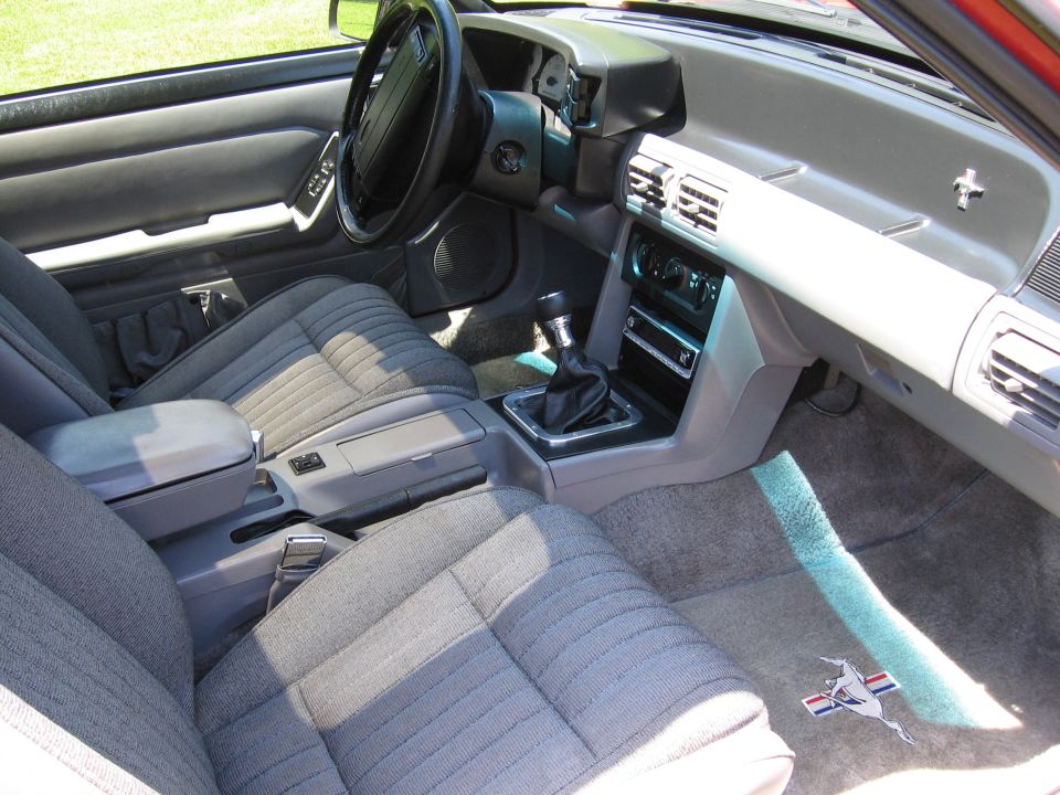 Interior of a 1993 Ford Mustang with grey cloth seats, manual transmission, and dashboard