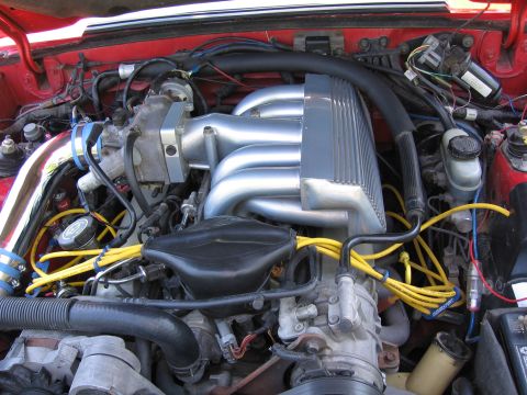 1967 Ford Mustang - Close-up view of a vehicle's engine bay, highlighting a chrome intake manifold and bright yellow spark plug wires.