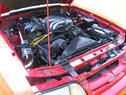 1967 Ford Mustang - The engine bay of a red vehicle, a chrome intake and "CAUTION FAN" shroud, is shown with a "SUPERMOTORS" watermark.