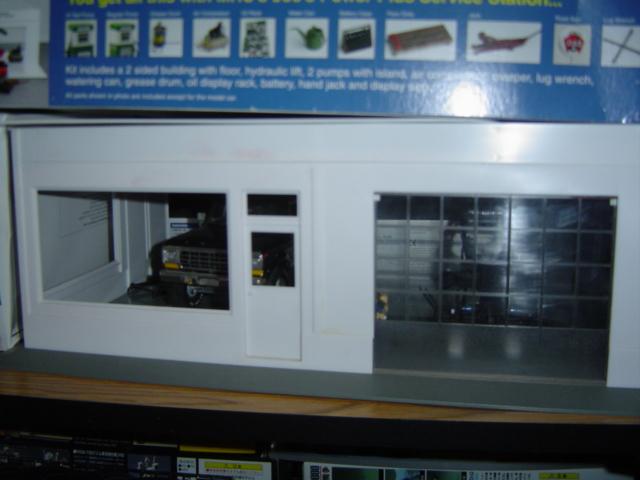 Model of a service station with a dark colored model car visible through the front window