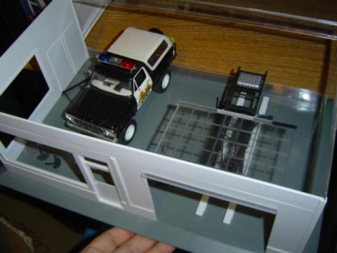 1979 Ford Bronco - A model police SUV is displayed inside a miniature garage diorama with a winch and lift.