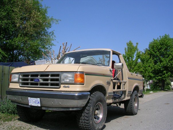 Tan Ford Bronco with off-road tires and roll cage, parked on a street