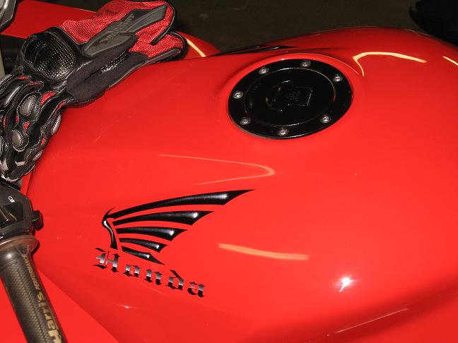 Red Honda motorcycle fuel tank with winged logo, locking gas cap and riding glove