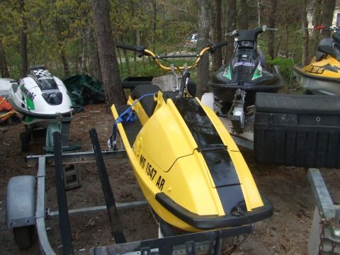 1995 Ford Mustang - Several jet skis are parked on trailers in a wooded area, with the closest one being yellow and black.