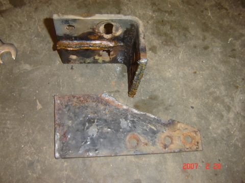1993 Ford Bronco - Two heavily rusted metal brackets, one appears broken, lie on a concrete surface. A wrench is visible to the left.