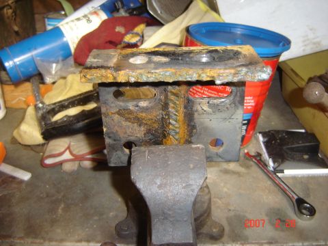 1993 Ford Bronco - A heavily rusted metal bracket is secured in a vise, surrounded by various tools and workshop supplies.