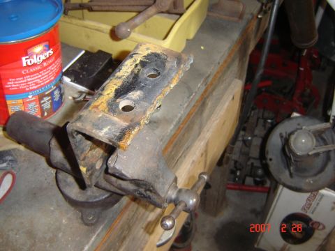 1993 Ford Bronco - A rusty metal bracket is clamped in a vise on a workbench, with a coffee can and other tools in the background.