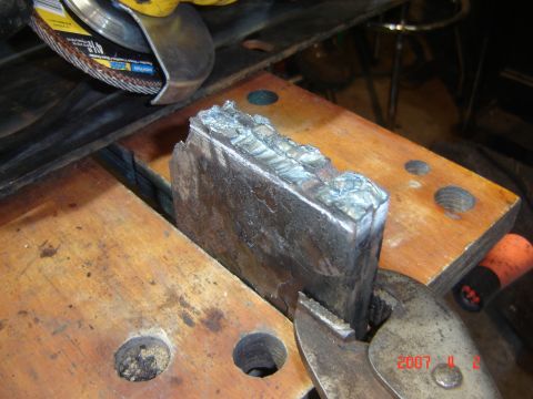 1993 Ford Bronco - A metal piece with visible welds is being cut by a grinder on a wooden workbench.