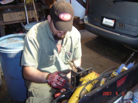 1993 Ford Bronco - Man working on a car part in a garage setting, with a blue bin and vehicle in background.