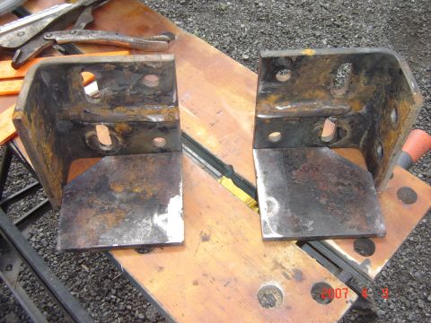 1993 Ford Bronco - Two heavily rusted metal brackets are shown resting on a wooden workbench.