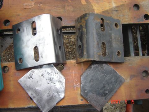 1993 Ford Bronco - Two metal brackets, one shiny and one rusted, sit with diamond-shaped plates on a wooden workbench.