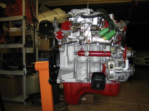 1987 Suzuki Samurai - Engine assembly displayed on a stand, a red oil pan and silver block with visible carburetor and wiring.