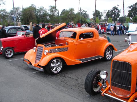1992 Ford Taurus - Orange 1935 Ford hot rod coupe at a car show, with other custom vehicles visible.