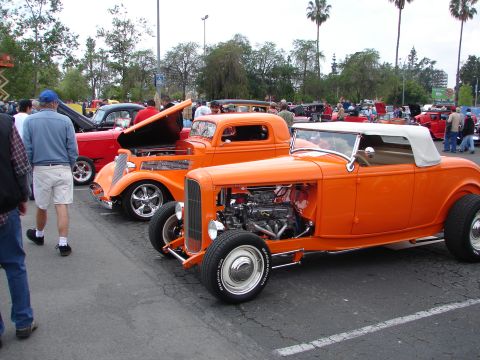 1992 Ford Taurus - A line of custom hot rod cars are displayed at an outdoor event.