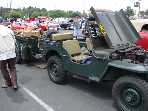 1992 Ford Taurus - A vintage military jeep and trailer are on display at a car show, with other classic cars in the background.