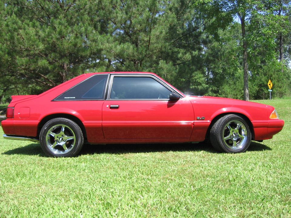 Red coupe car with black trim and chrome wheels parked on grass