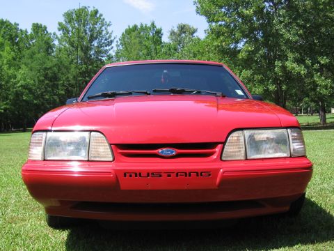 1967 Ford Mustang - Front view of a red Ford Mustang, likely from the late 1980s or early 1990s, with the model name visible on the bumper.
