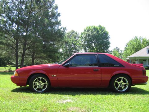 1967 Ford Mustang - Side view of a red 1993 Ford Mustang coupe with a "5.0" badge, parked on a grassy lawn.