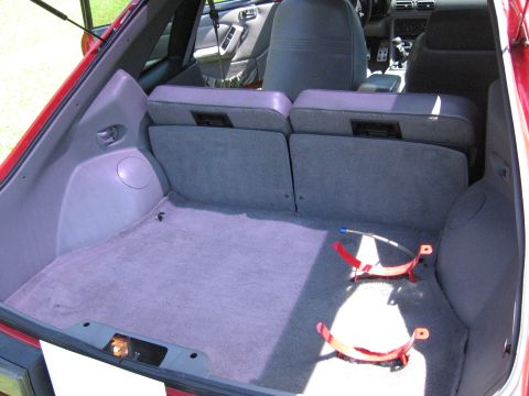 1967 Ford Mustang - The interior of a red hatchback reveals a carpeted cargo space and folded rear seats, with red brackets visible on the floor.