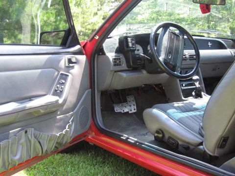 1967 Ford Mustang - The interior of a red car is shown, a manual transmission and aftermarket pedals.