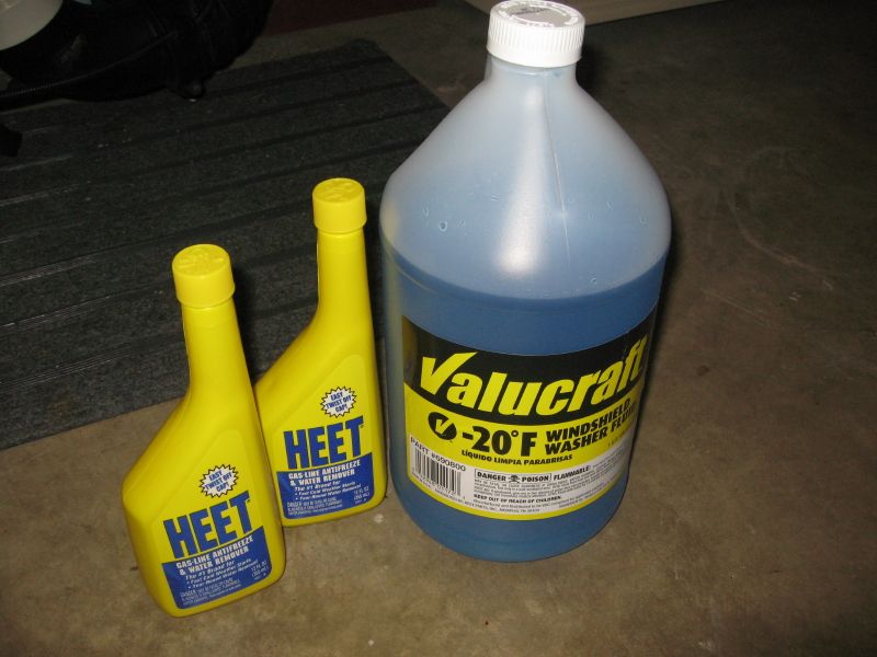 Two HEET gas-line antifreeze bottles and a gallon of Valucraft -20°F windshield washer fluid on a concrete floor