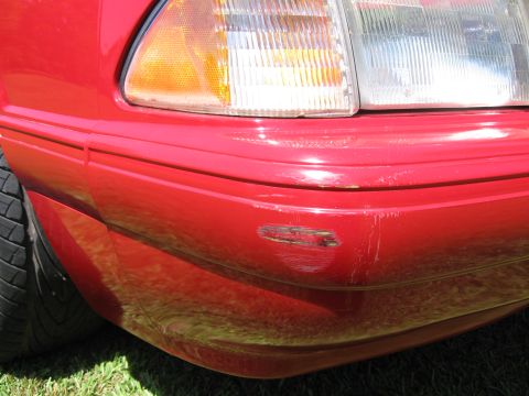 1967 Ford Mustang - The front corner of a red car shows damage to the bumper and fender area.