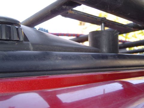 1996 Ford Explorer - Detail of a roof rack mounting point on a red vehicle, showing a black rubber seal and metal rack components.