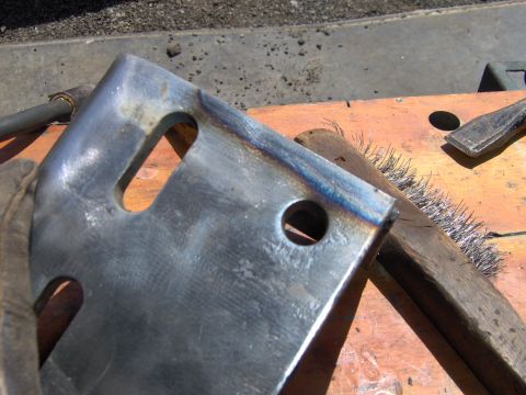 1993 Ford Bronco - Metal bracket with weld marks, next to a wire brush and chisel on a wooden surface.