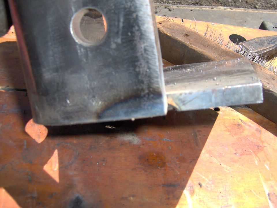 Close-up of a metal bracket with a hole, resting on wood