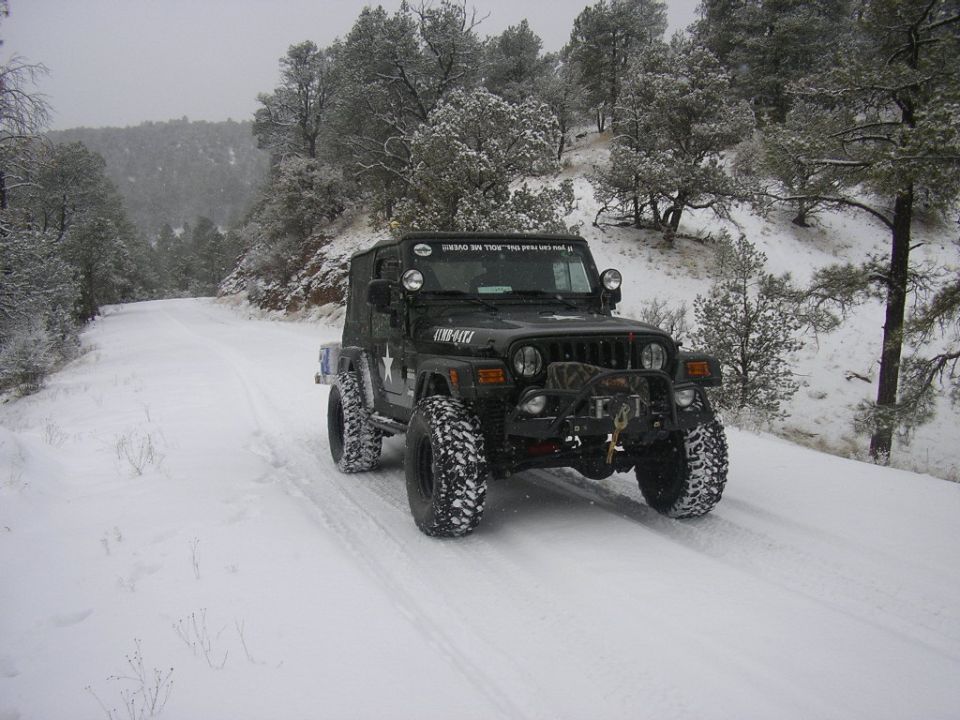 Black Jeep Wrangler with large tires on a snowy road