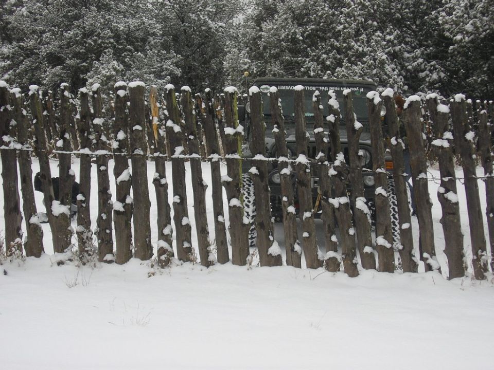 2004 Jeep TJ behind a rustic wooden fence with snow on the logs and trees