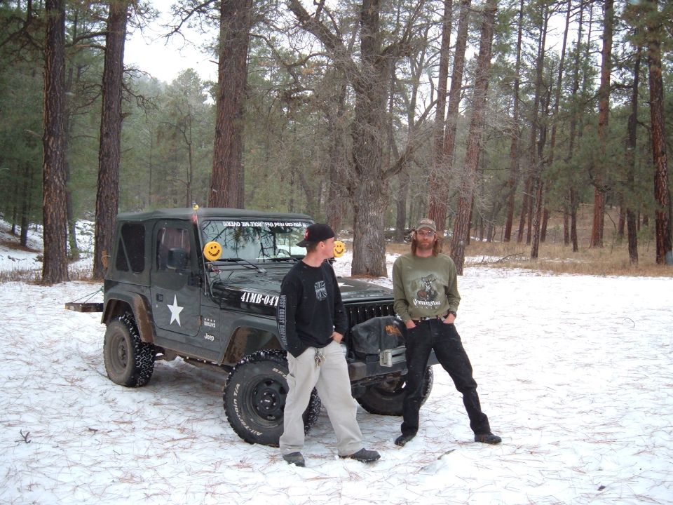 Green Jeep Wrangler with a white star on the door, parked in the snow with two men standing nearby