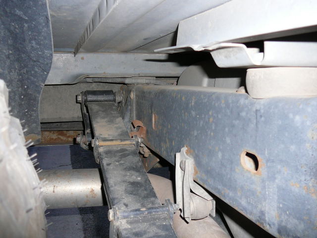 Leaf spring attached to a vehicle frame, with a tire and exhaust pipe visible