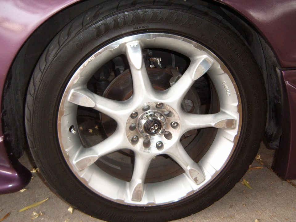 Silver multi-spoke alloy wheel with Dunlop tire on a purple car