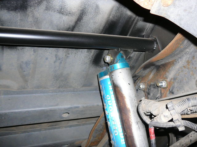 Close-up of blue off-road shocks and a black sway bar mounted to a vehicle's undercarriage