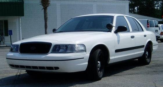 White sedan parked outside a building, with a palm tree and a white van in the background
