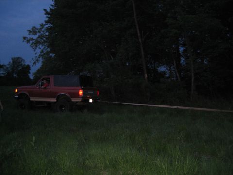 1990 Ford Bronco - A red 1990 Ford Bronco is seen from the side, being towed through a grassy area as daylight fades.