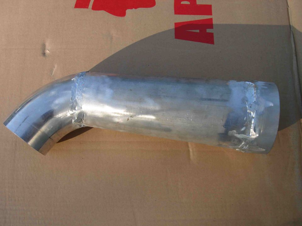 Welded aluminum intake pipe with elbow and stepped larger end on cardboard
