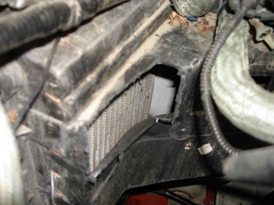 Close-up of a car's AC condenser unit with surrounding black plastic housing and hoses