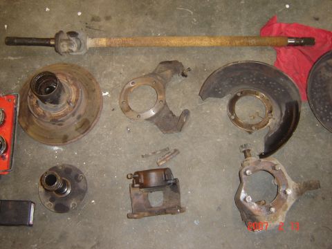 1993 Ford Bronco - Various rusty vehicle parts, including brake rotors, calipers, and a drive shaft, are laid out on a concrete surface.