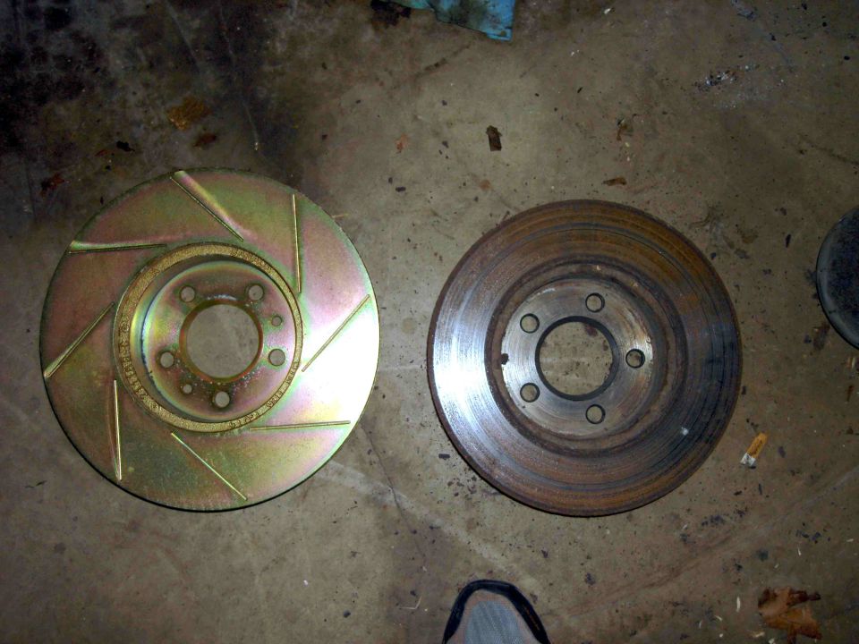 New slotted brake rotor next to old rusty one on concrete floor