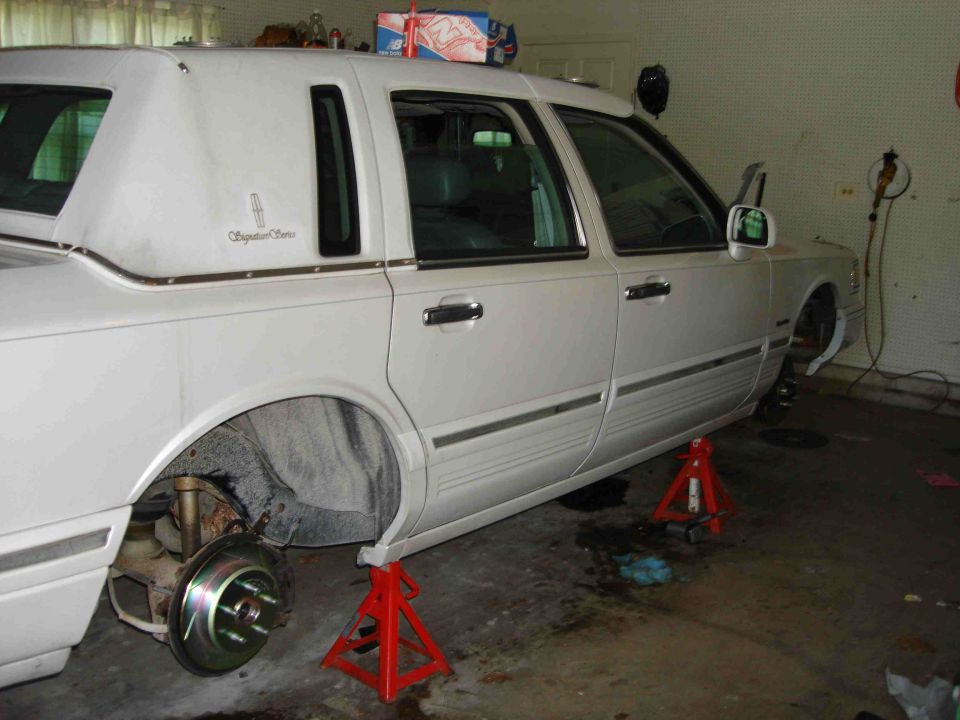White Lincoln Town Car Signature Series on jack stands in a garage, wheels off